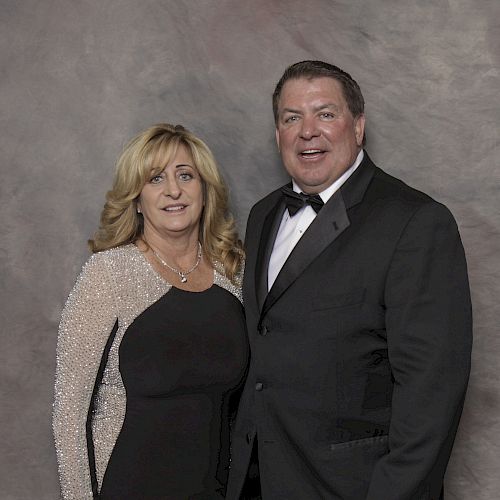 A man and woman stand together, both dressed formally. The woman wears a sparkling black and silver dress; the man wears a black tuxedo.