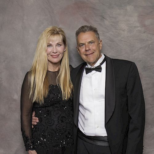 A man and woman are posing together for a formal portrait, with the man in a tuxedo and the woman in a black dress.