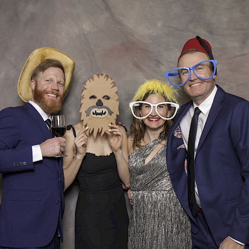 Four people in costumes with props, including oversized glasses, a yellow hat, a mask, a fez, and a cowboy hat, posing for a fun photo.